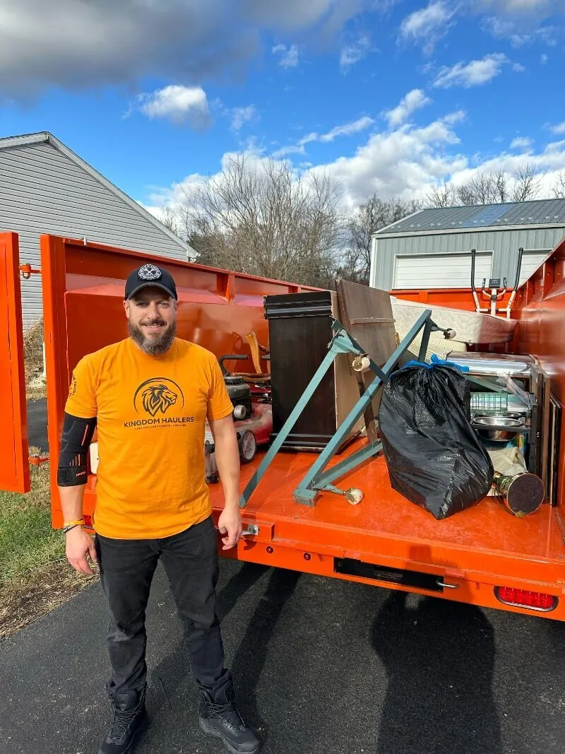 Mike, owner of Kingdom Haulers, standing beside a loaded orange dump trailer