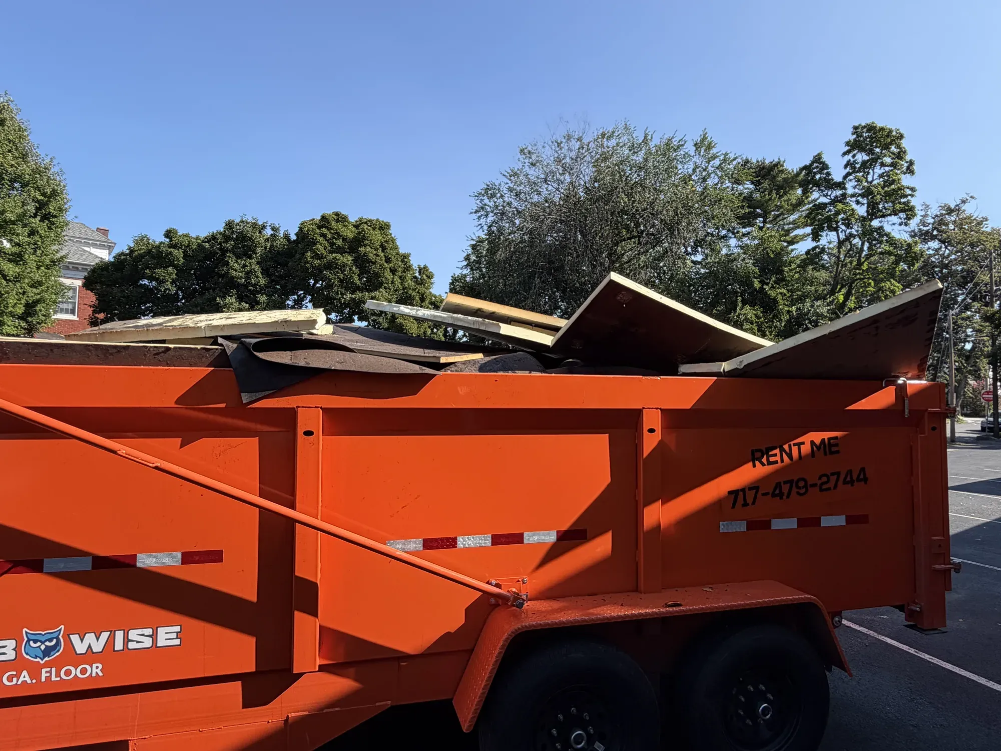 Orange trailer dumpster parked in a lot, piled with roofing debris and decking