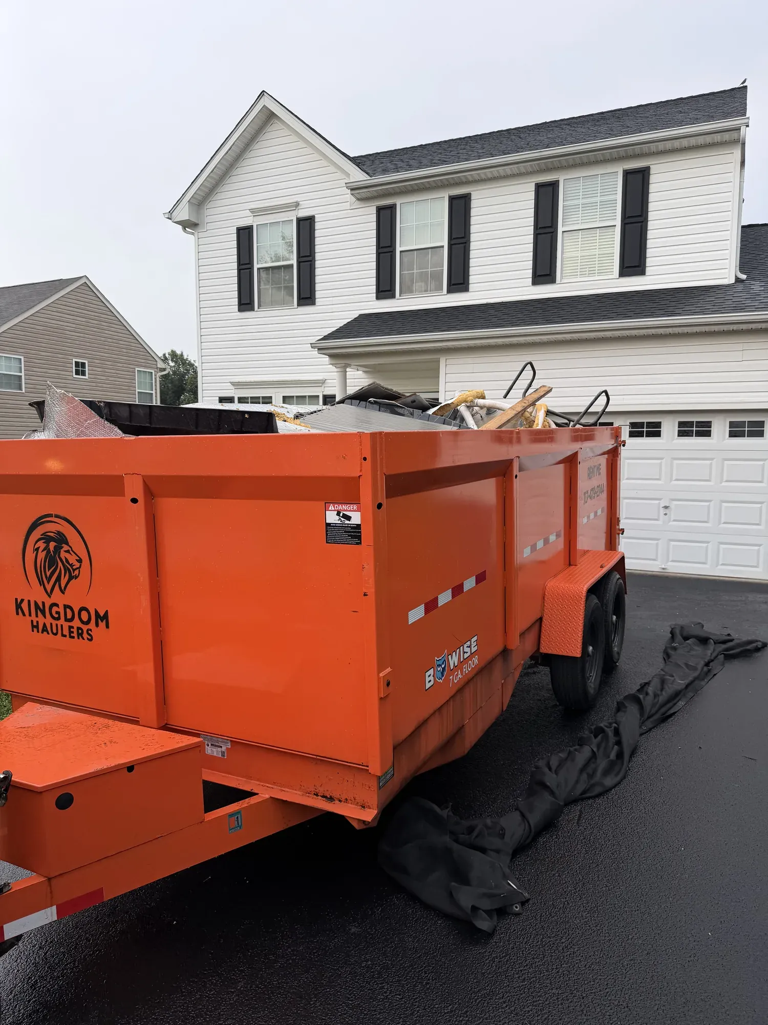 Kingdom Haulers branded dump trailer, loaded with debris, in front of a two-story house