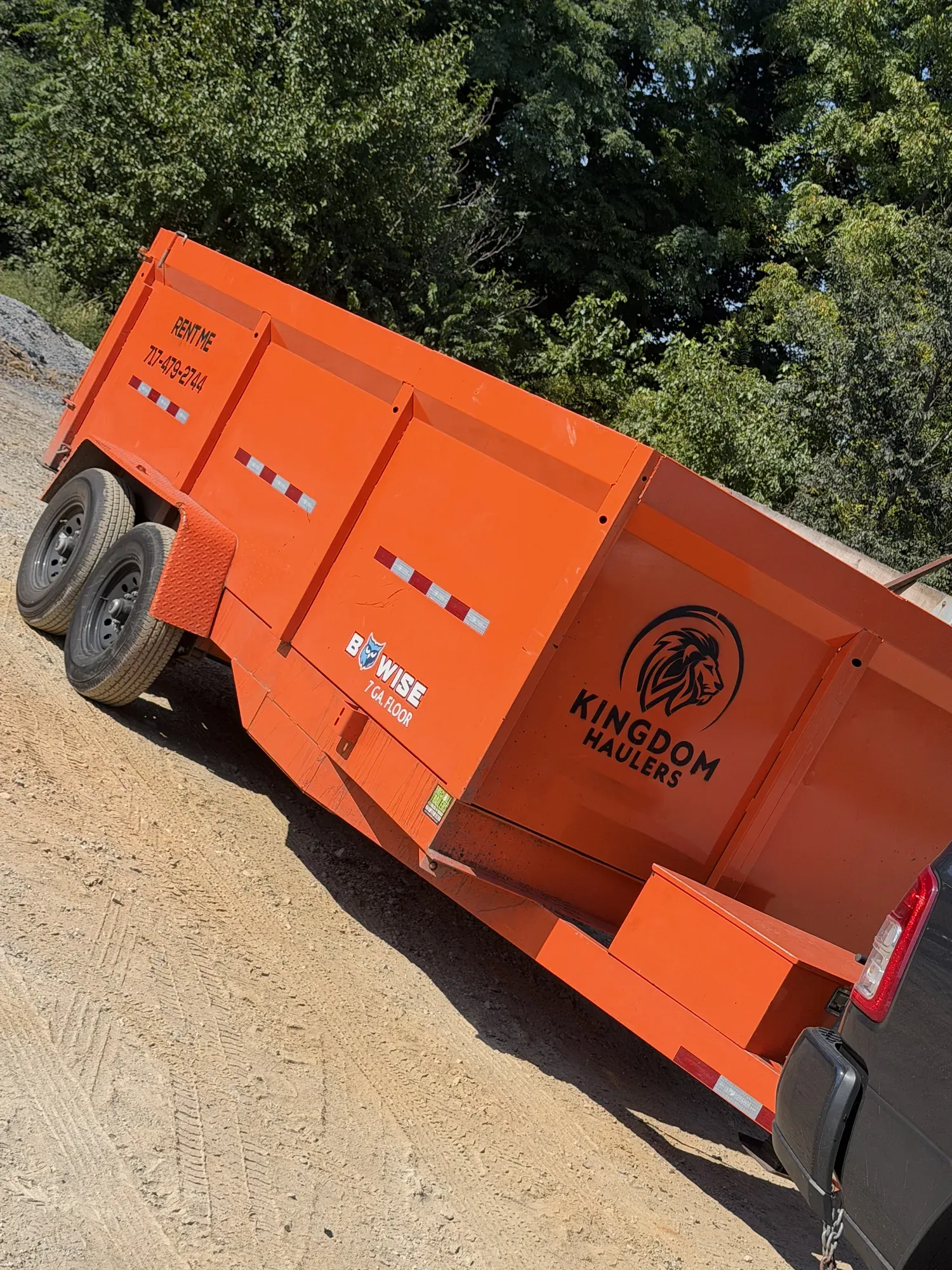 Orange Kingdom Haulers branded dump trailer hitched up on a dirt jobsite