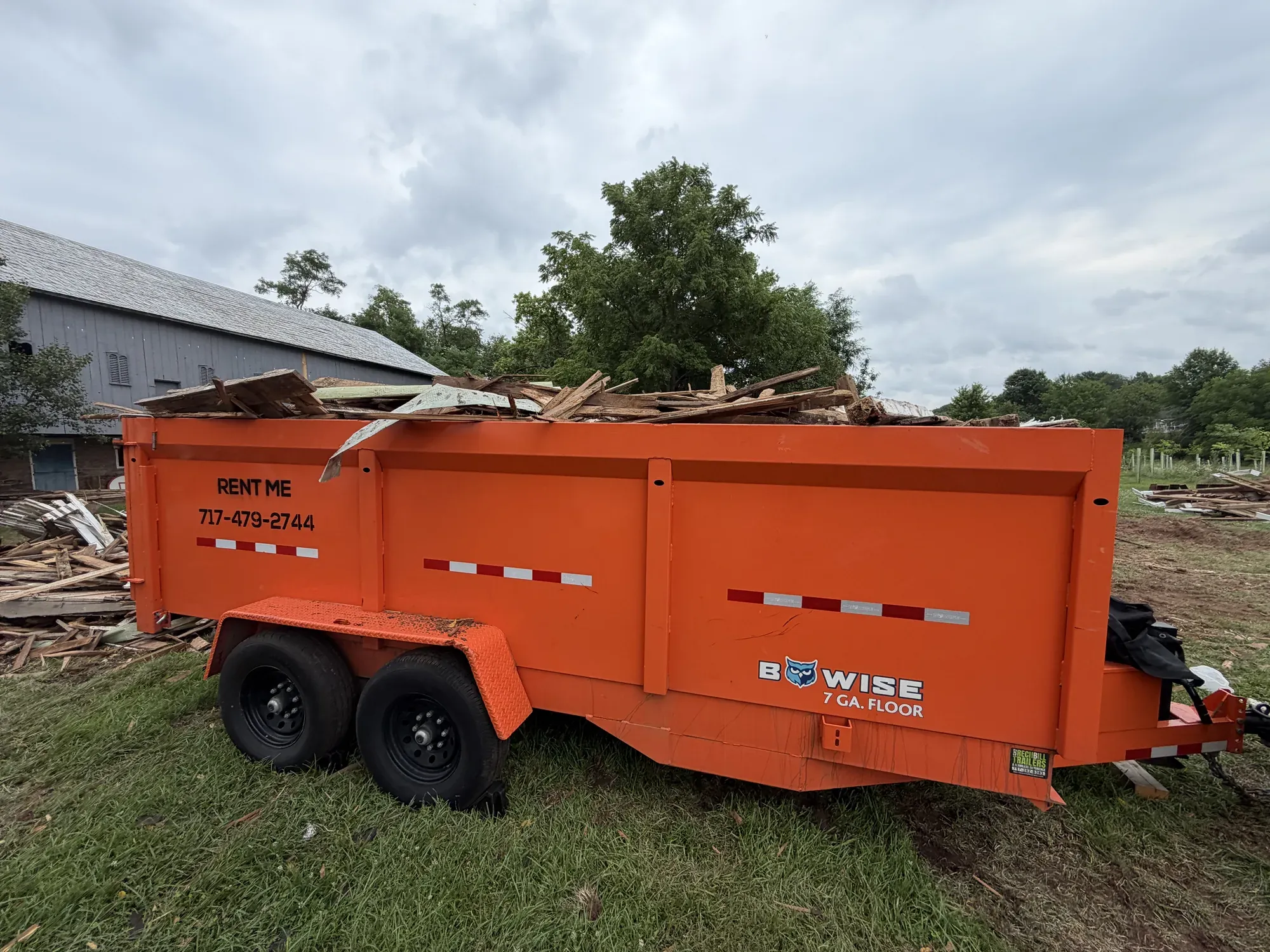 Orange RENT ME dump trailer piled high with demolition lumber on a jobsite