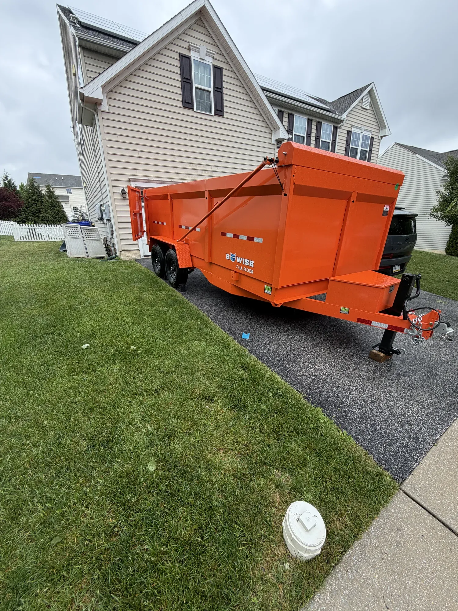 Orange dump trailer with its bed raised, unloading in a residential driveway