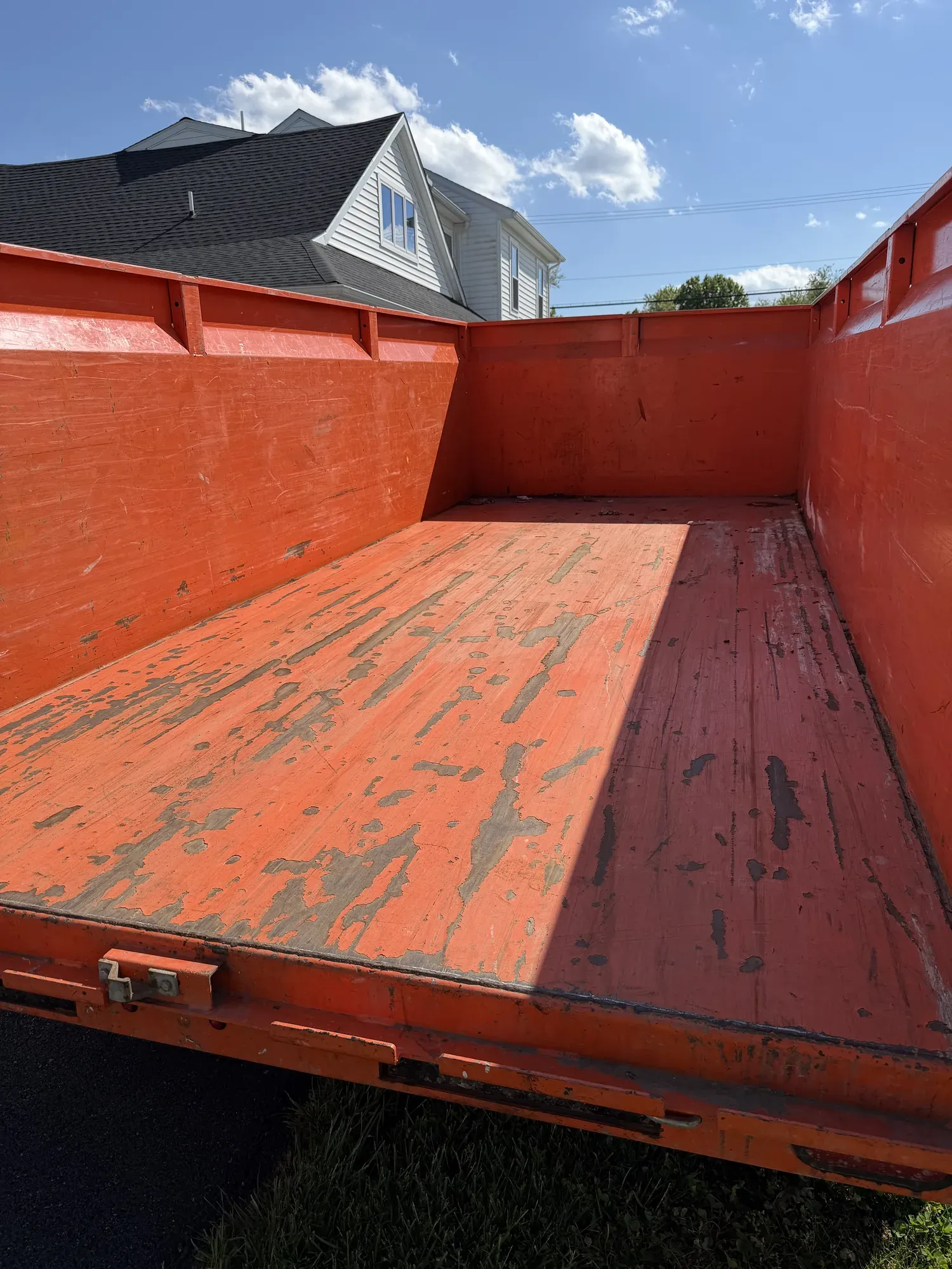 Empty steel bed of an orange dump-trailer dumpster, ready to load