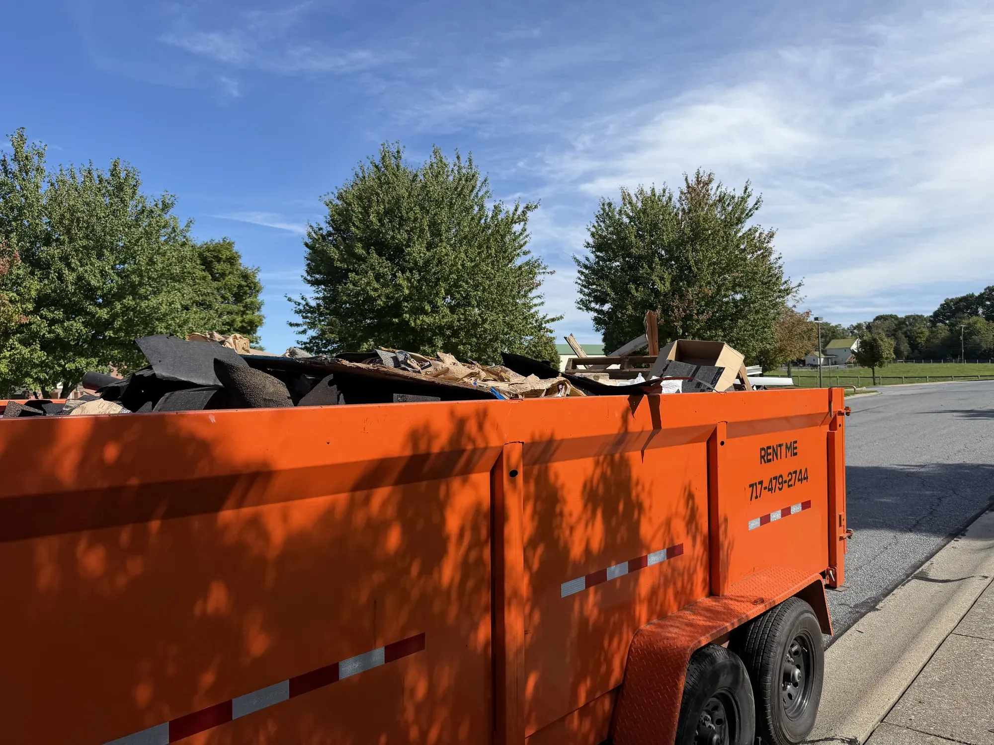 Loaded orange RENT ME trailer dumpster parked at the curb on a residential street