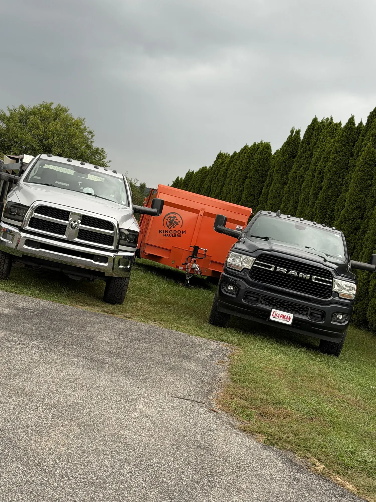 Two Kingdom Haulers pickups with an orange trailer dumpster parked between them